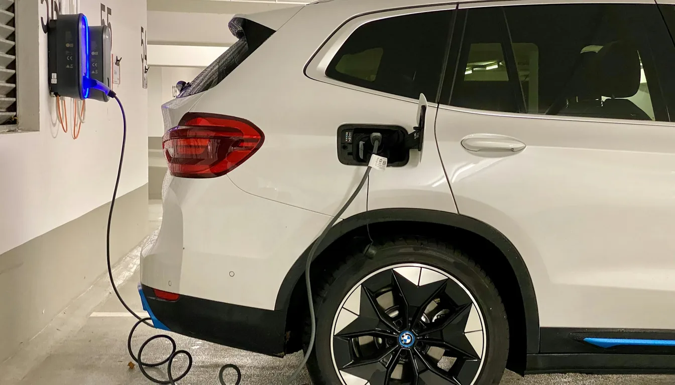 A white electric SUV charging from a wall-mounted station in a parking garage